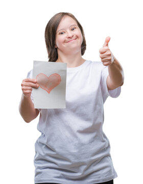 Young adult woman with down syndrome holding red heart card over isolated background happy with big smile doing ok sign, thumb up with fingers, excellent sign