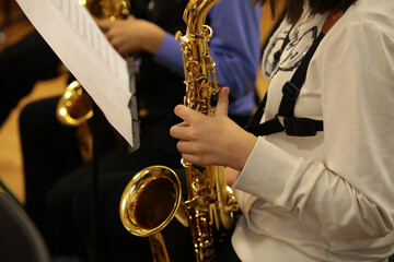Girl student musician playing the saxophone with a musical instrument in her hands at the rehearsal...