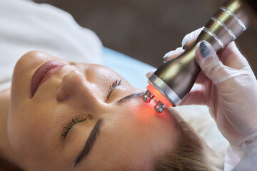 A cosmetologist in rubber gloves does the rf-lifting procedure on the face. In the background, the...
