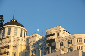 Fototapeta premium Fragment of modern white building and incomplete moon in blue sk