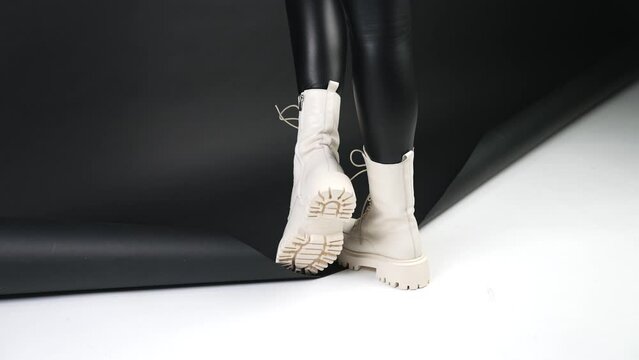 White combat boots on tractor soles. Model in black pants standing with her back to camera on a black and white backdrop.