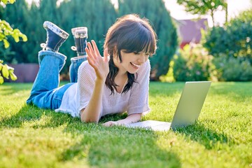 Young female lying outdoor on grass with laptop talking with friends using video call