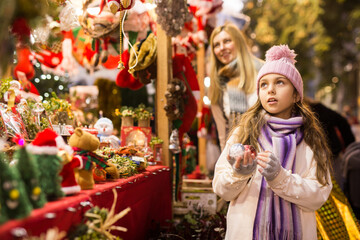 Enthusiastic teenager girl picking tree decorations at street christmas market