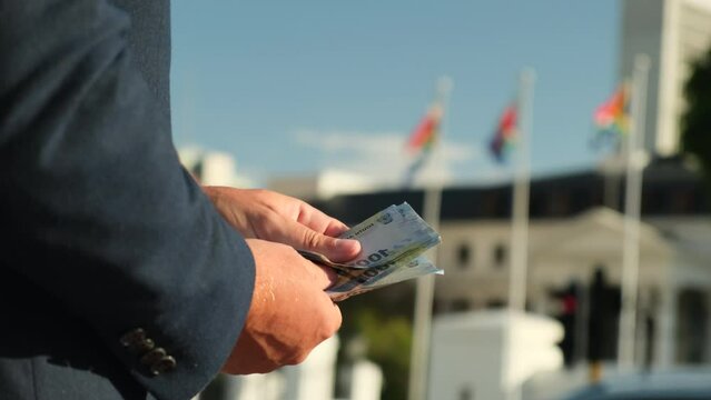 man counts South African rands money in hands. close-up of the hands of a european businessman in a business suit and white shirt holding money against the background of the flag of south africa
