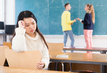 Portrait of frustrated Asian girl sitting apart in class, having conflict with fellows students
