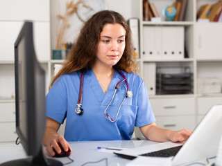 Young positive brunette female doctor with stethoscope working in medical office