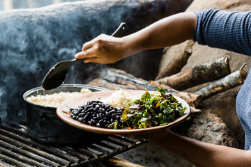 Hands of an unrecognizable woman serving a plate of rice with beans and salad in a traditional...