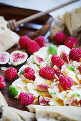 Butter board topped with fresh raspberries, figs, sliced almonds, basil leaves, and drizzled with honey. Selective focus with blurred foreground and background.