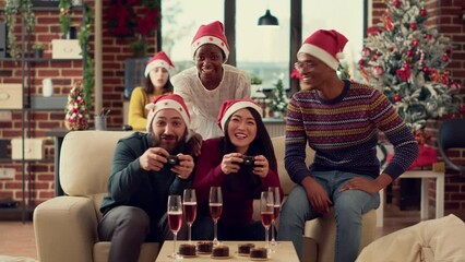 Diverse coworkers playing video games on console during christmas party celebration in office. Using controller to play gaming competition with colleagues, celebrating winter holiday. Tripod shot.