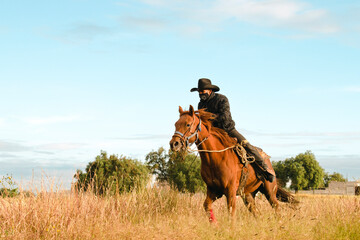 Mexican man riding a horse in a field at dawn 