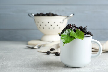 Cup of delicious ripe black mulberries on grey table, space for text