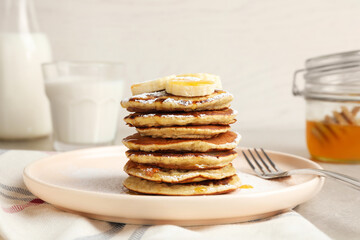 Fototapeta na wymiar Plate of banana pancakes with honey and powdered sugar served on table, closeup