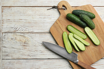 Whole and cut fresh ripe cucumbers on white wooden table, flat lay. Space for text
