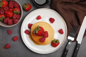 Tasty pancakes served with fresh berries and honey on grey table, flat lay