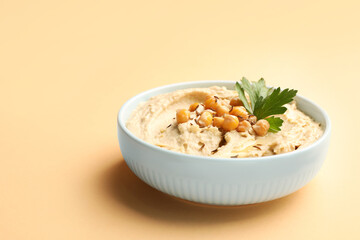 Bowl of tasty hummus with chickpeas and parsley on beige background. Space for text