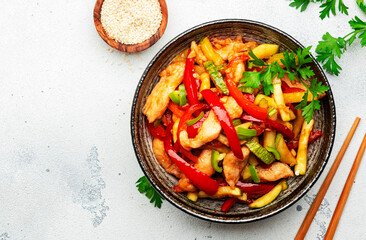 Asian cuisine, stir fry with chicken, red paprika pepper and zucchini bowl. White kitchen table background, top view, copy space