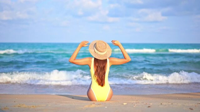 Back View of Lonely Woman in Swimsuit Sitting on Beach in Front of Tropical Sea and Raising Arms Full of Joy, Slow Motion