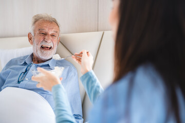 Elderly patient having support health care service by nurse in a old people home providing residential care by bringing breakfast to her senior man occupant, medical care of retirement caucasian man