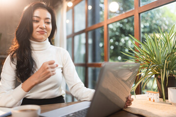 Happy laughing business woman using laptop computer for distant work. Hipster young Asian manager female working in the cafe connected to wireless internet connection, concept of freelance work