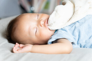 毛布を咥えながらお昼寝をする赤ちゃん