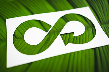 ecology and sustainability, circular economy symbol on paper cutout with tropical leaf underneath it