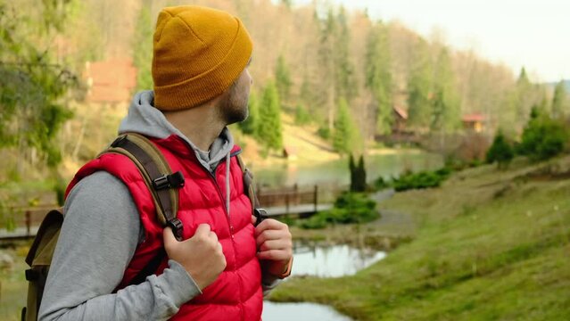 ale traveller in warm clothes from back, standing at mountain lake coast enjoying the view of the Alps in Austria. Como Lake. Tourist with backpack sitting on river bank at sunset. summer travel