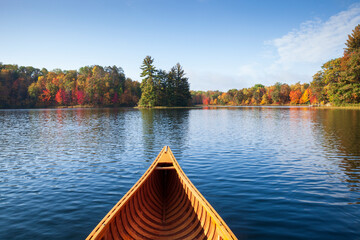 Wooden canoe moves on a blue lake with trees in autumn color and a small island in northern...