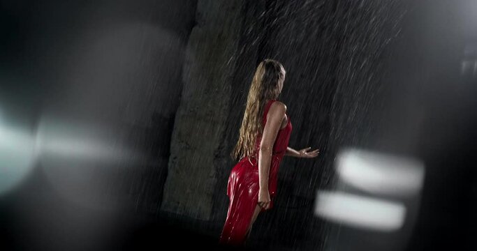Tempting Young Woman Dancer in Red Dress Performing in the Rain in Dark Studio