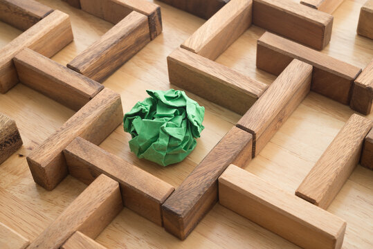 Green crumpled paper find escape exit in wooden maze background. Business strategy planning for successful company target, creative new idea, problem solution, innovation thinking concept.