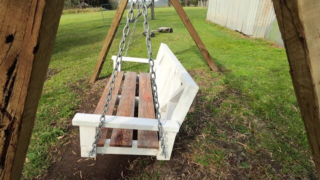 Empty wooden chair swings in the breeze in large backyard or rural farm