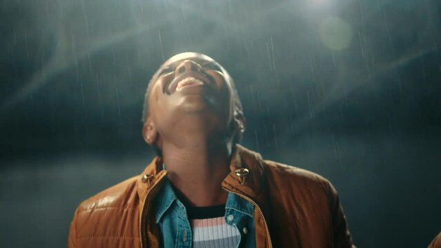 Freedom, rain and dance with a black woman playing in the water during winter at night outside. Free, joy and weather with a young female dancing, screaming and shouting outdoor alone with a smile