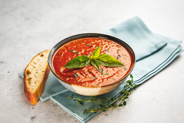Bowl of fresh homemade tomato basil soup with fresh herbs and slice of focaccia bread on a blue napkin