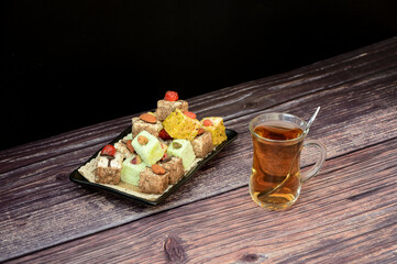 A rectangular plate with an assortment of oriental sweets and a glass cup of hot tea on a wooden table.