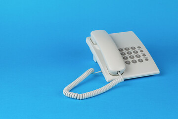 A white telephone with gray buttons on a blue background. - obrazy, fototapety, plakaty