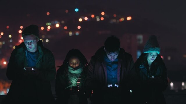 Night, rooftop and gaming friends with smartphone for online video game mobile app with bokeh city lights in the dark. Happy social media, gen z group of people with 5g cellphone networking web chat