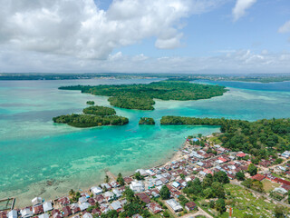 Obraz premium Aerial view of village near beautiful beach with small island in the background in Maluku, Indonesia