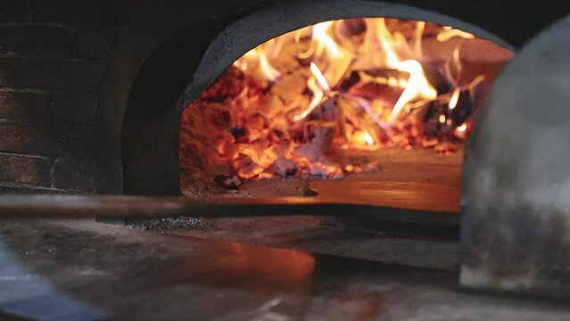 Fresh traditional rustical pizza with salami, green peperoni, cheese and tomatoe souce get shoved into oven fired by wood with beutiful flames