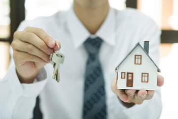 Real estate agent holding house model and keys to consult client.