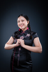 Happy Chinese New Year or Lunar Year. An Asian Chinese young woman poses wearing traditional cheongsam dress. Half height. Isolated on dark background.