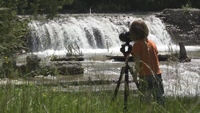 Little cameraman filming the waterfall in the mountain landscape