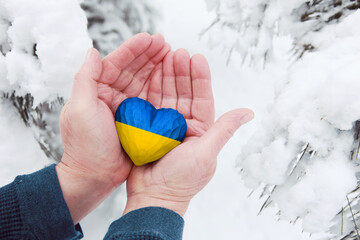 Man hands holding a carved wooden heart with colors of Ukraine flag in winter