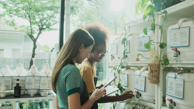 Two young female shopkeepers check stock of natural organic products in reusable containers shelves at refill store, zero waste, plastic-free grocery shop, and eco-friendly, sustainable lifestyles.