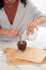 Woman adding milk in cup with coffee