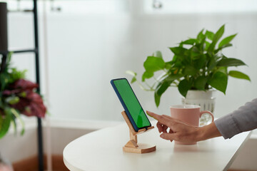 Side view of hand of young businesswoman pointing at green screen of smartphone