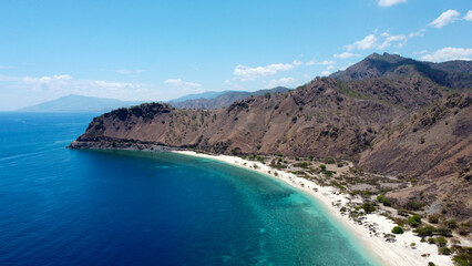 Fototapeta na wymiar Aerial drone view of beautiful white sandy beach with green and blue ocean water and dry mountainous landscape in Dili, Timor Leste, Southeast Asia