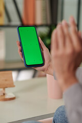 Hand of young woman holding smartphone with blank green screen