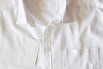 Blank price label tag paper card on white natural linen shirt. Clothes label tag mockup template...
