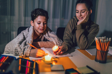 Boy and girl studying in low light with a burning candle.  Power outage, energy crisis concept.
