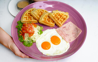 Hands holding plate with eggs with ham and salad and belgian waffles close up