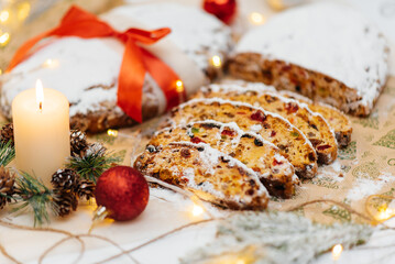 Traditional German Christmas stollen made of dried fruits and nuts, sprinkled with powdered sugar on the background of a Christmas decor with candles. A festive treat.